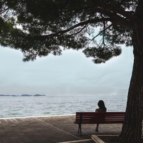 a nude woman in a fetal position beneath blue water who is sinking deeper